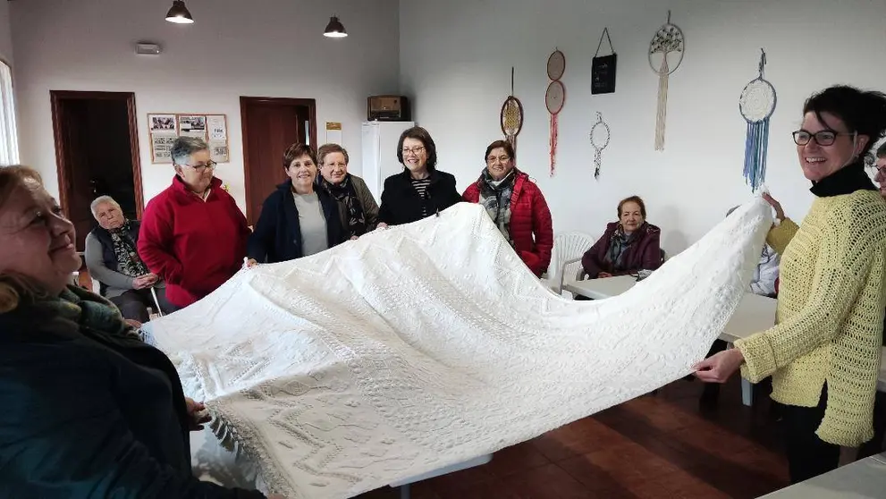 Mulleres participantes do obradoiro da Escola Rural de Saúde da Limia amosan unha das pezas tecidas.